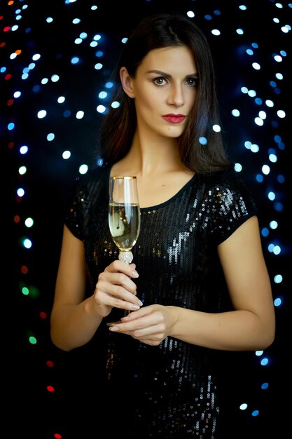 Photo portrait d'une belle jeune femme tenant une flûte à champagne contre des lumières éclairées