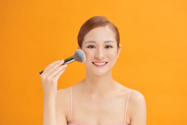 Portrait d'une belle jeune femme tenant un pinceau à la main et appliquant de la poudre sur son visage avec un pinceau.