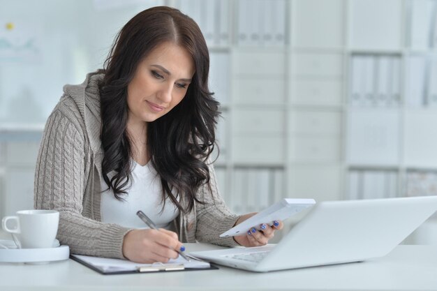 Portrait d'une belle jeune femme travaillant au bureau avec un ordinateur portable