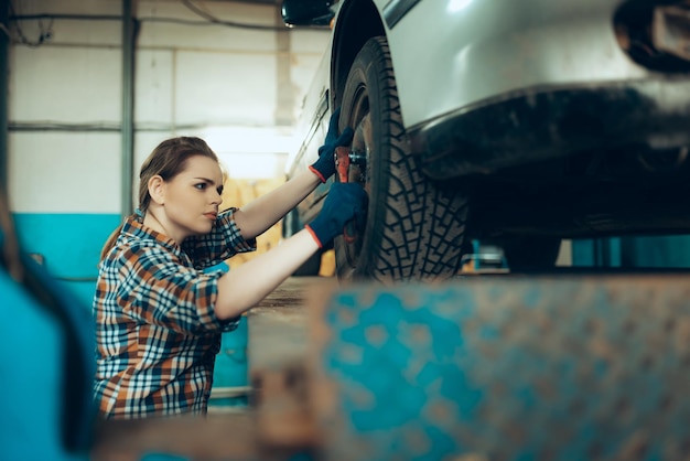 Portrait d'une belle jeune femme travaillant comme mécanicien automobile changeant de roue de voiture au service automobile à l'intérieur