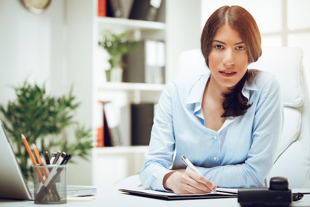 Portrait d'une belle jeune femme travaillant à son bureau au bureau et regardant la caméra.