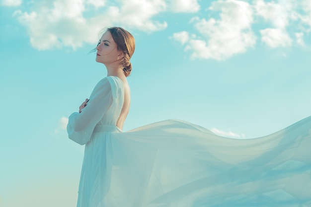 Portrait d'une belle jeune femme vêtue d'une longue robe blanche contre le ciel. Robe au vent