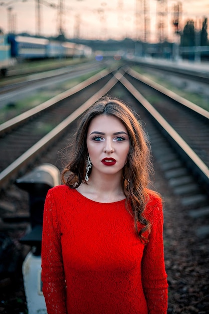Portrait belle jeune femme vêtue d'une longue robe rouge se tient près du chemin de fer