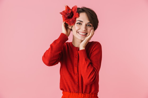 Portrait d'une belle jeune femme vêtue d'une robe rouge debout isolé, posant avec une fleur