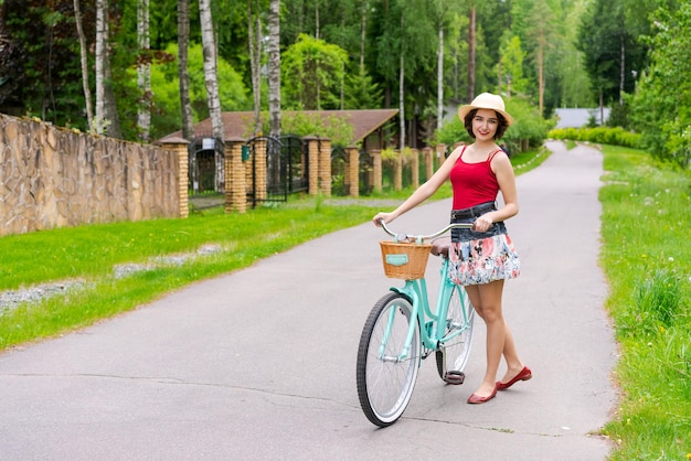 Portrait belle jeune fille au chapeau avec vélo dans la rue à la campagne