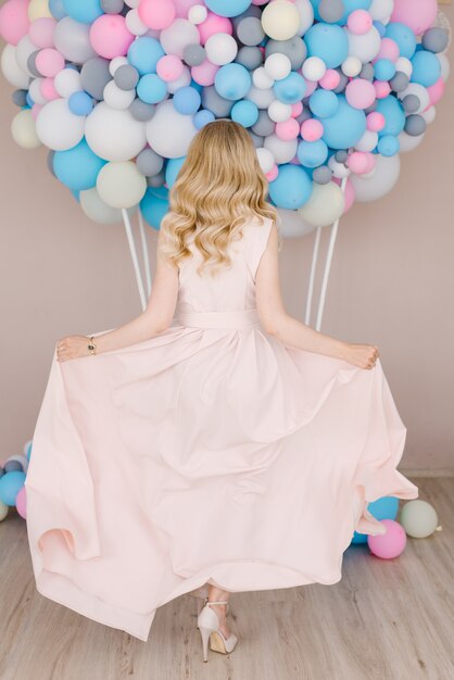 Portrait d'une belle jeune fille aux cheveux blonds bouclés en pleine croissance. Debout en arrière et dansant dans une robe légère sur fond de ballons blancs et bleus.