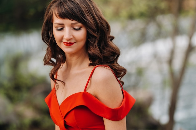 Portrait d'une belle jeune fille aux longs cheveux bruns, dans une longue robe rouge dans la nature.