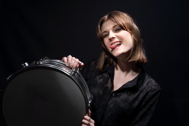 Portrait d'une belle jeune fille de batteur souriante en noir tenant une caisse claire posant sur un fond noir