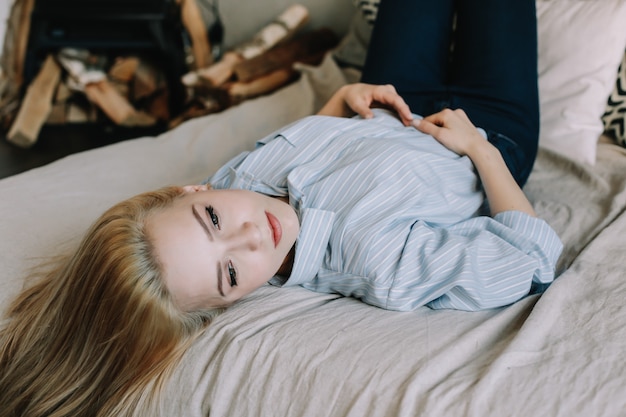 portrait d'une belle jeune fille blonde au lit le matin à la maison dans un intérieur scandinave bonjour style de vie