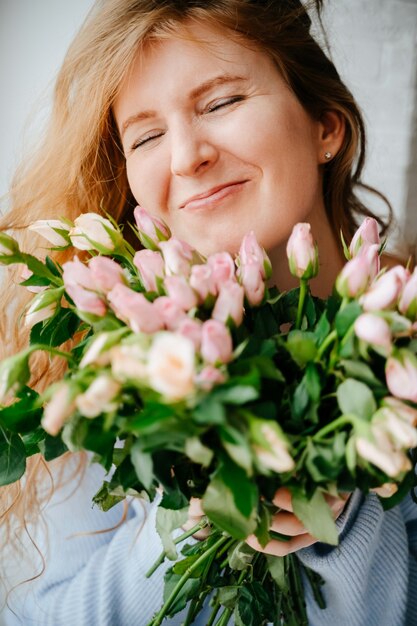 Portrait d'une belle jeune fille avec un bouquet de roses près de la fenêtre. Cheveux roux bouclés.