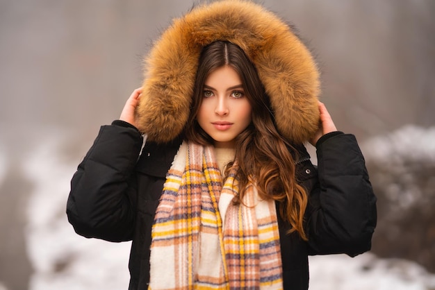 Portrait de la belle jeune fille brune en manteau d'hiver avec capuche en fourrure et écharpe chaude.