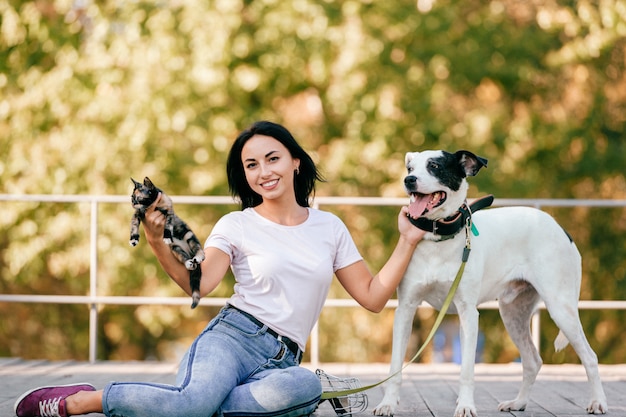 Portrait de la belle jeune fille brune avec petit chat et gros chien chien assis en plein air dans le parc