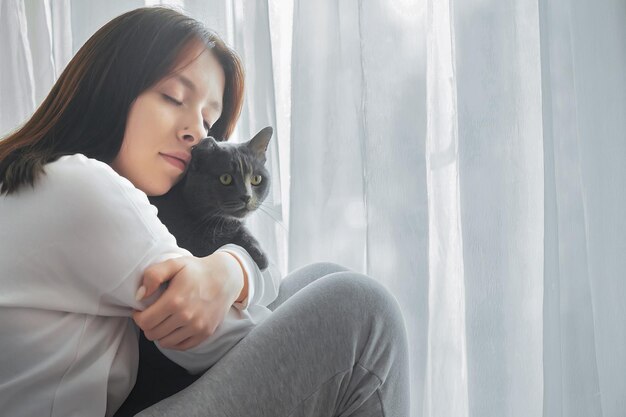 Portrait d'une belle jeune fille avec un chat près de la fenêtre