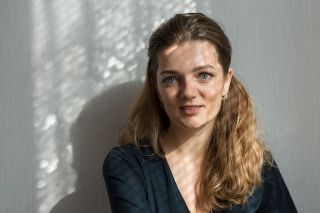 Portrait d'une belle jeune fille dans une pièce sur fond de mur gris avec des ombres naturelles