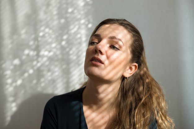 Portrait d'une belle jeune fille dans une pièce sur fond de mur gris avec des ombres