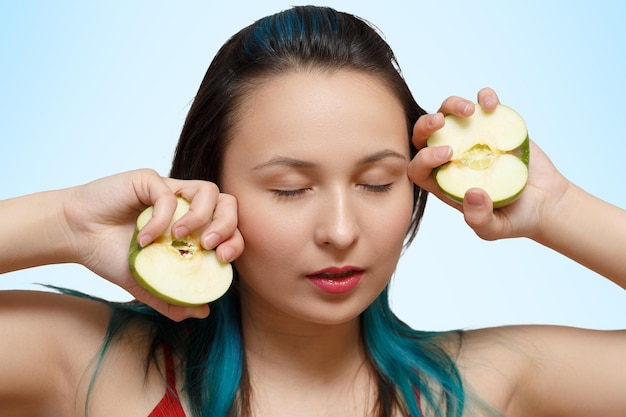 Portrait d'une belle jeune fille avec deux moitiés de pommes dans ses mains sur un fond bleu