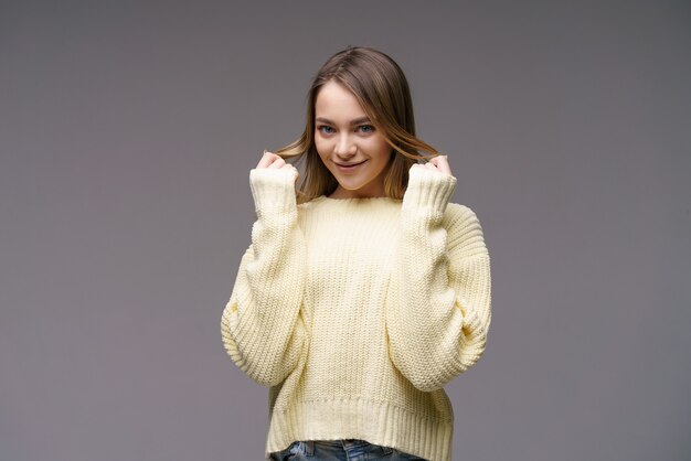 Portrait d'une belle jeune fille d'ethnie caucasienne dans un pull jaune sur fond gris c...