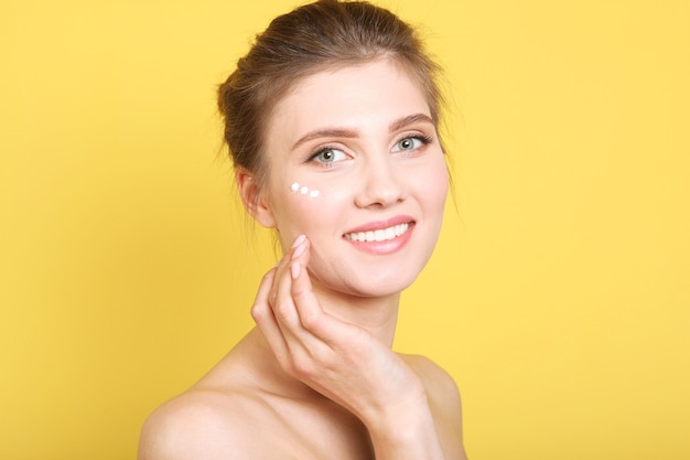 Portrait d'une belle jeune fille sur fond coloré qui utilise une crème bienveillante