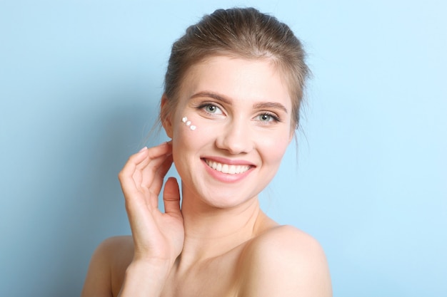 Portrait d'une belle jeune fille sur fond coloré qui utilise une crème bienveillante