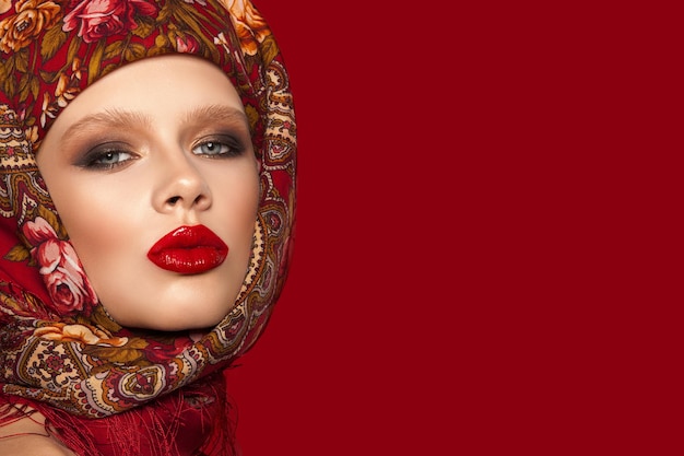 Portrait d'une belle jeune fille avec un foulard sur la tête maquillage lumineux et lèvres rouges fond rouge