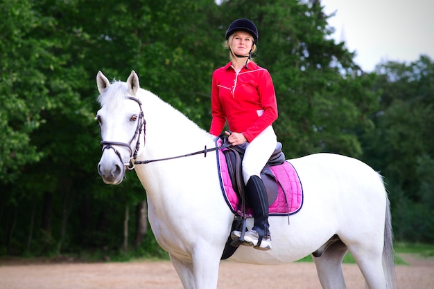 Portrait d'une belle jeune fille heureuse cavalier équestre sur cheval blanc en casque et polo