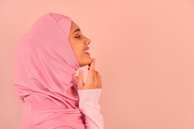 Portrait d'une belle jeune fille musulmane portant un hijab rose sur fond beige Vue latérale Espace de copie