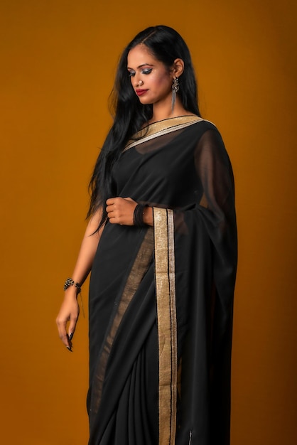 Portrait d'une belle jeune fille portant un sari noir traditionnel posant sur un fond marron