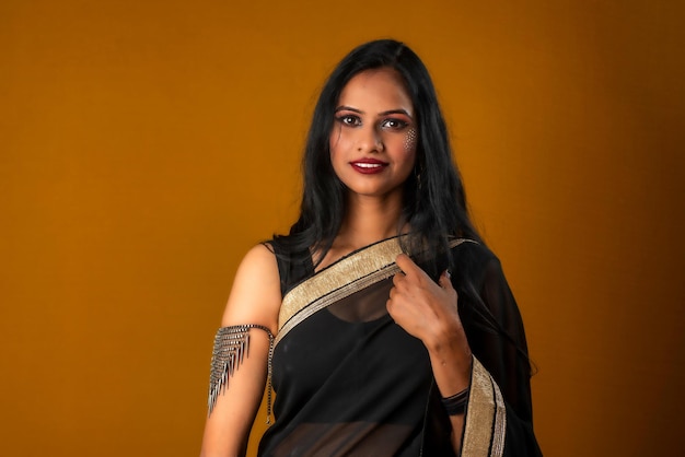 Portrait d'une belle jeune fille portant un sari noir traditionnel posant sur un fond marron