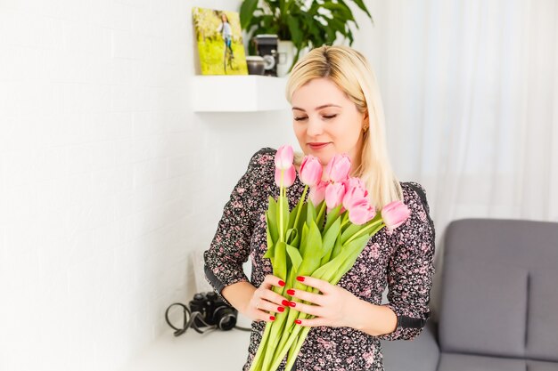 Portrait d'une belle jeune fille en robe tenant un gros bouquet de tulipes à la maison sur le canapé