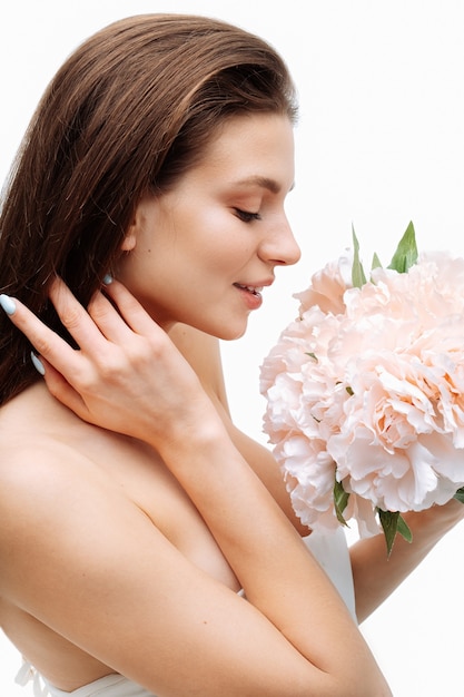 Portrait belle jeune fille souriante et posant avec des fleurs artificielles sur un mur blanc en robe blanche