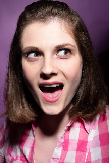 Photo portrait d'une belle jeune fille surprise dans une chemise à carreaux sur fond rose