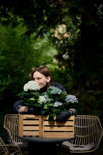 Portrait d'une belle jeune fleuriste étreignant un bouquet de belles fleurs dans un pot en bois sur la table dans le jardin