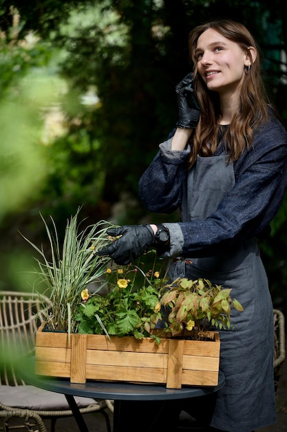 Portrait d'une belle jeune fleuriste en tablier qui plante des fleurs dans un pot dans le jardin