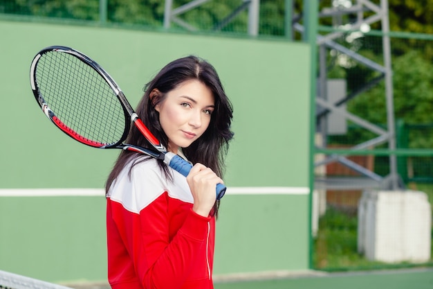 Portrait d'une belle jeune joueuse de tennis en vêtements de sport tenant une raquette de tennis sur le court.