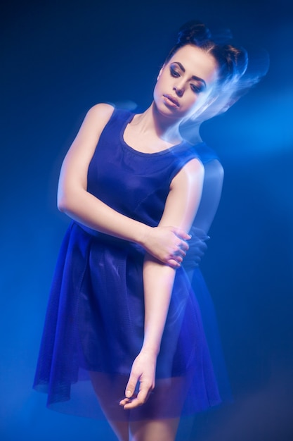 Portrait de la belle jeune mannequin posant en robe bleue sur fond bleu.Longue exposition