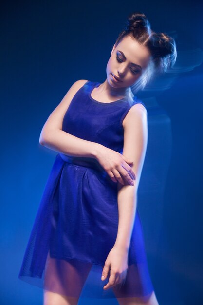 Portrait de la belle jeune mannequin posant en robe bleue sur fond bleu.Longue exposition
