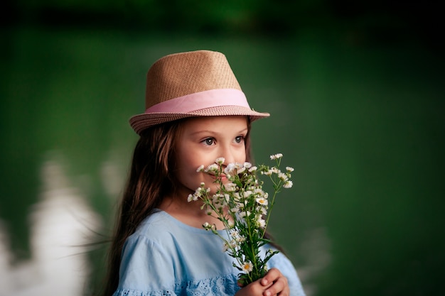 Portrait d'une belle jolie fille de 7 à 8 ans dans la nature, et l'enfant tient des fleurs dans ses mains, contre le mur de la rivière.