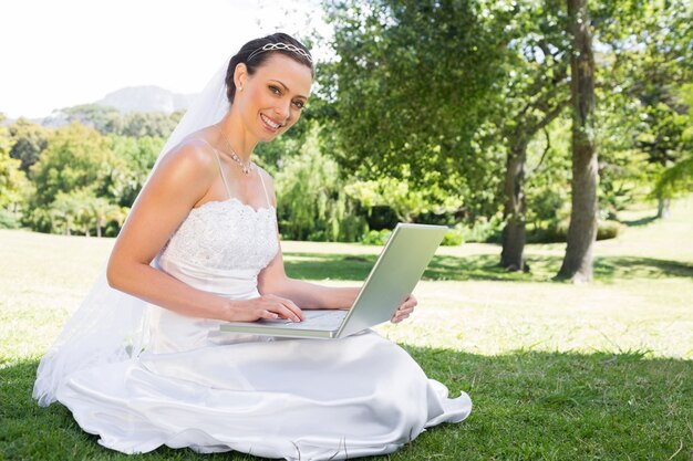 Portrait de la belle mariée à l&#39;aide d&#39;ordinateur portable tout en étant assis sur l&#39;herbe au jardin