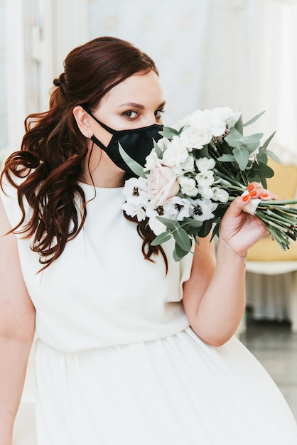 Portrait d'une belle mariée avec un bouquet dans un masque de protection médicale sur son visage. Mariage pendant la période de pandémie Covid-19.