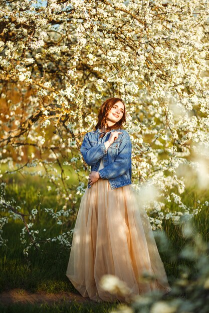 Portrait d'une belle mariée. Concept de mariage. Mariage élégant. Grande lumière du coucher du soleil. Elle porte une veste en jean bleu, une robe. Jardin fleuri au printemps.