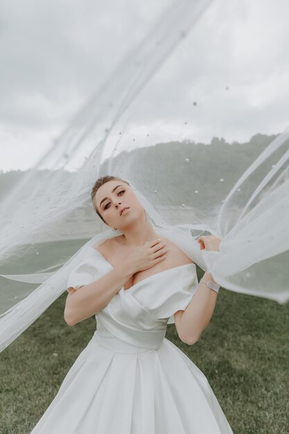 Portrait de la belle mariée en robe de mariée beige avec une coiffure bouclée moderne et un voile marchant sur g