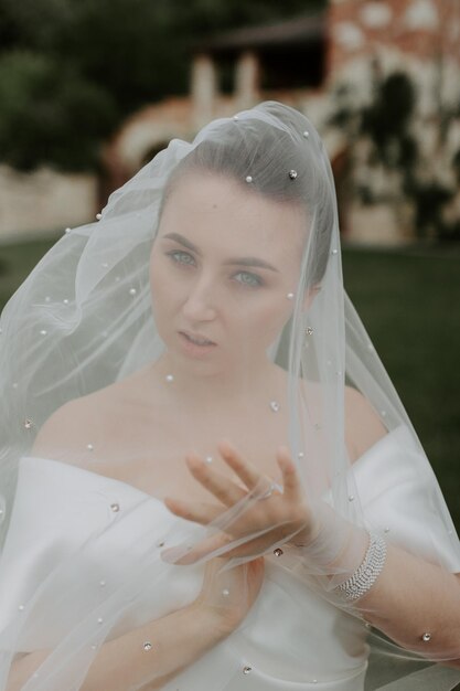 Portrait de la belle mariée en robe de mariée beige avec une coiffure bouclée moderne et un voile marchant sur g