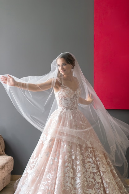 Portrait de la belle mariée en robe vintage blanche qui pose sous le voile en studio