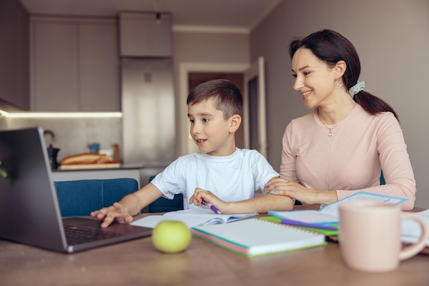 Portrait d'une belle mère caucasienne avec un petit fils adolescent faisant ses devoirs sur un ordinateur portable