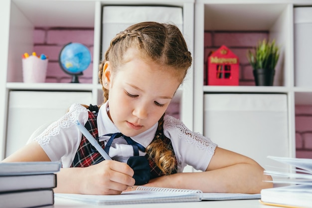 Portrait belle petite écolière positive assise à son bureau et faisant ses devoirs Concept de retour à l'école