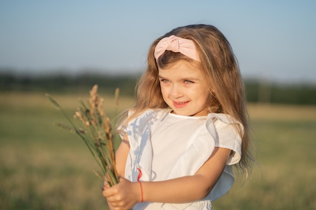 Portrait d'une belle petite fille aux cheveux blonds l'enfant se promène dans le champ et recueille un bou
