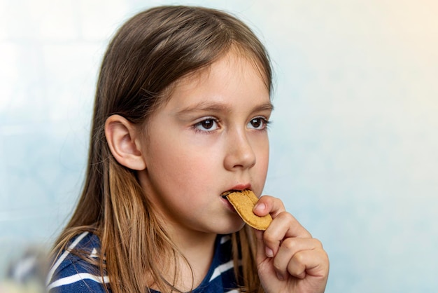 Portrait d'une belle petite fille aux cheveux longs, mord des biscuits sur fond bleu