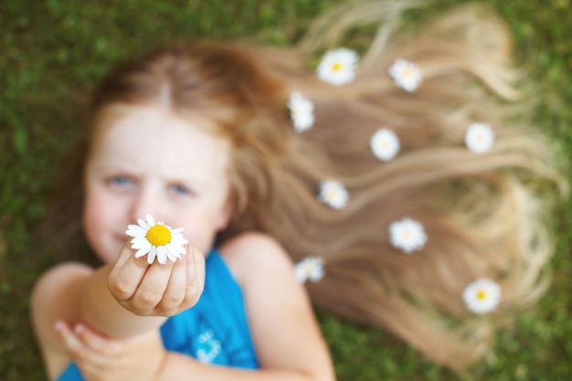 Portrait d'une belle petite fille aux cheveux roux en bonne santé avec des fleurs de camomille allongée sur l'herbe