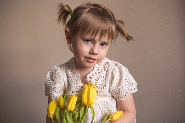 Un portrait d'une belle petite fille avec un bouquet de fleurs de tulipes jaunes