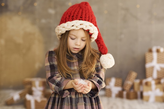 Un portrait de belle petite fille avec un chapeau de Noël restant près de cadeau sur le fond